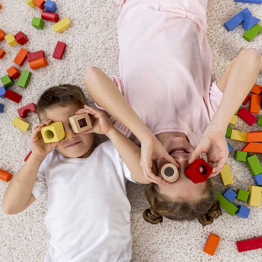 Una niña y un niño en el suelo jugando con bloques de juguetes.